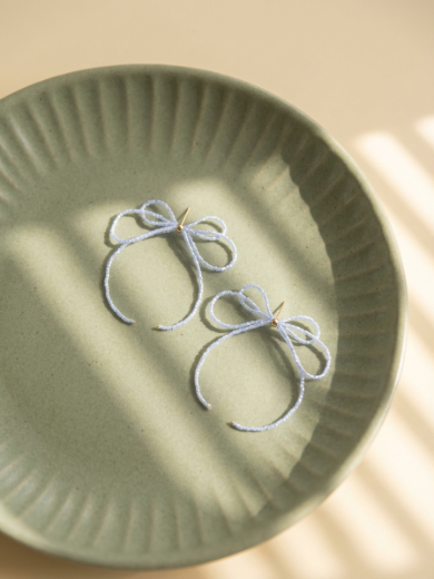Pale blue bow earrings resting in a green ceramic dish
