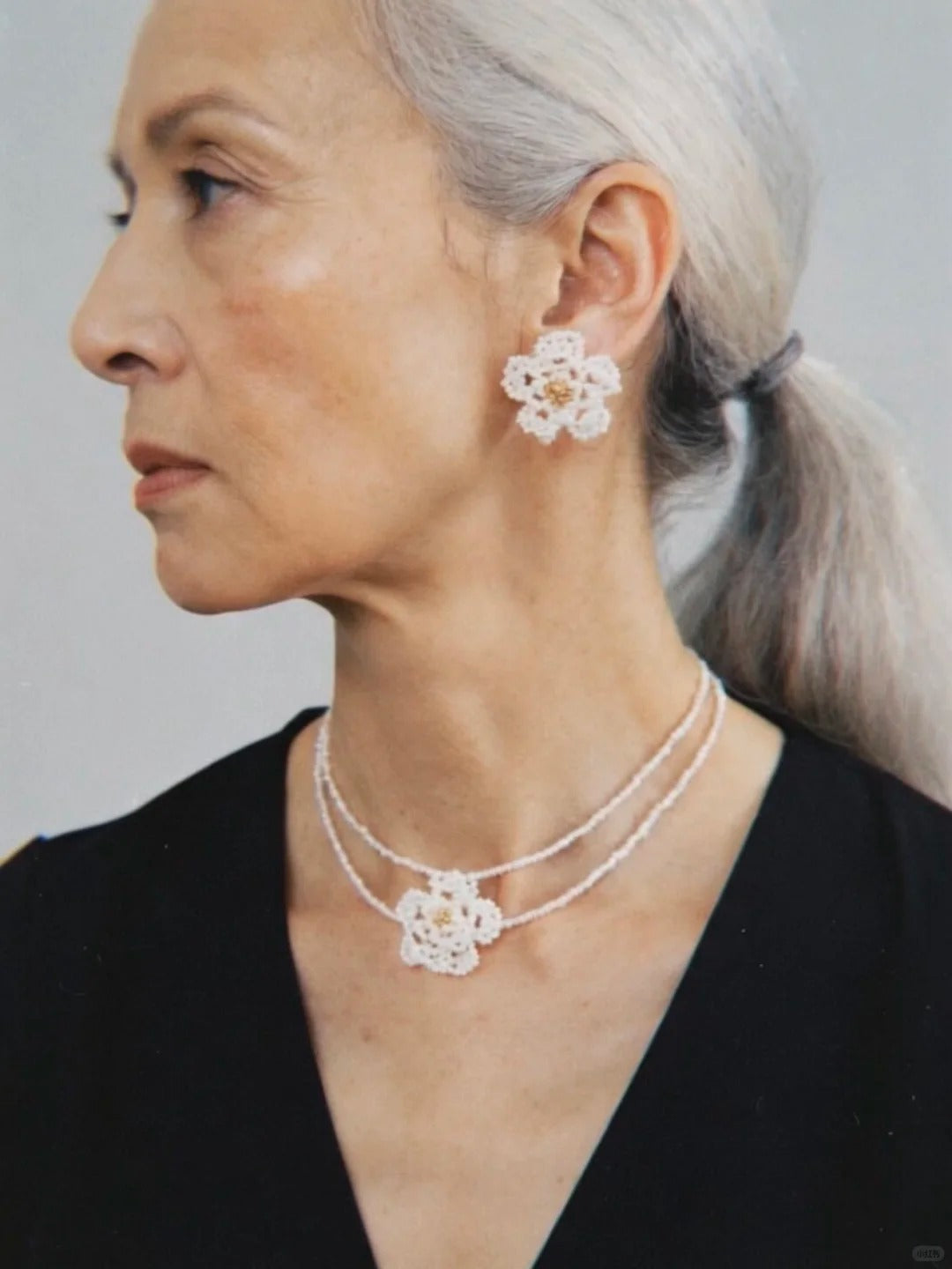 Side profile with swept-back hair, black neckline, and a Fullice Camellia flower set
