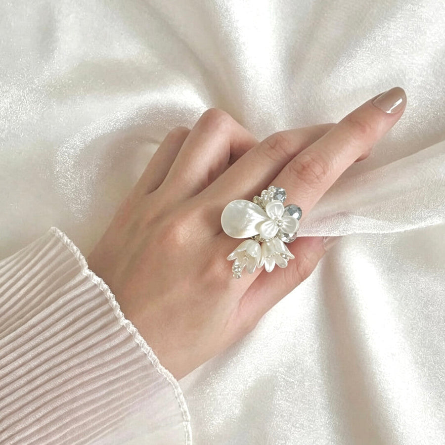 Hand wearing a Fullice Magnolia flower ring resting on clean white satin
