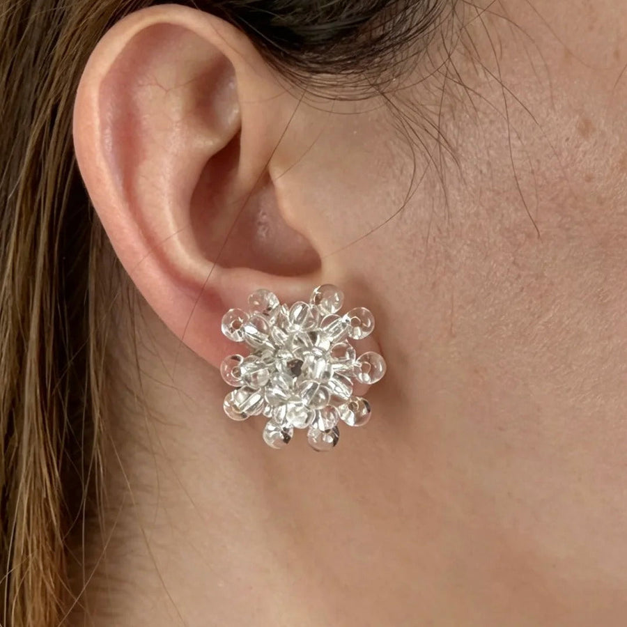 Close-up of a compact Fullice Tears flower stud earring worn on the ear